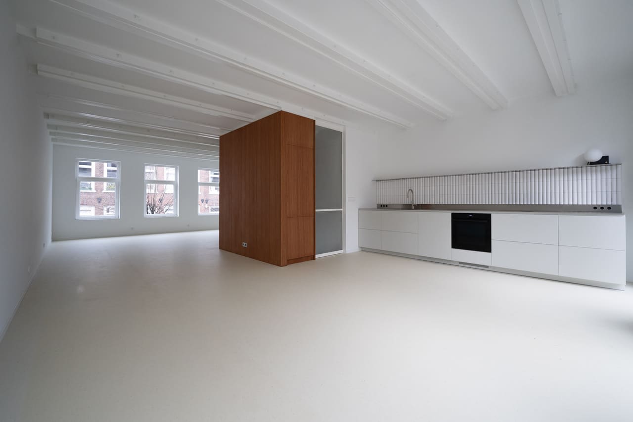 Dezelfde ruimte na de renovatie: greeploze keuken met stalen werkblad en houten kastenvolume